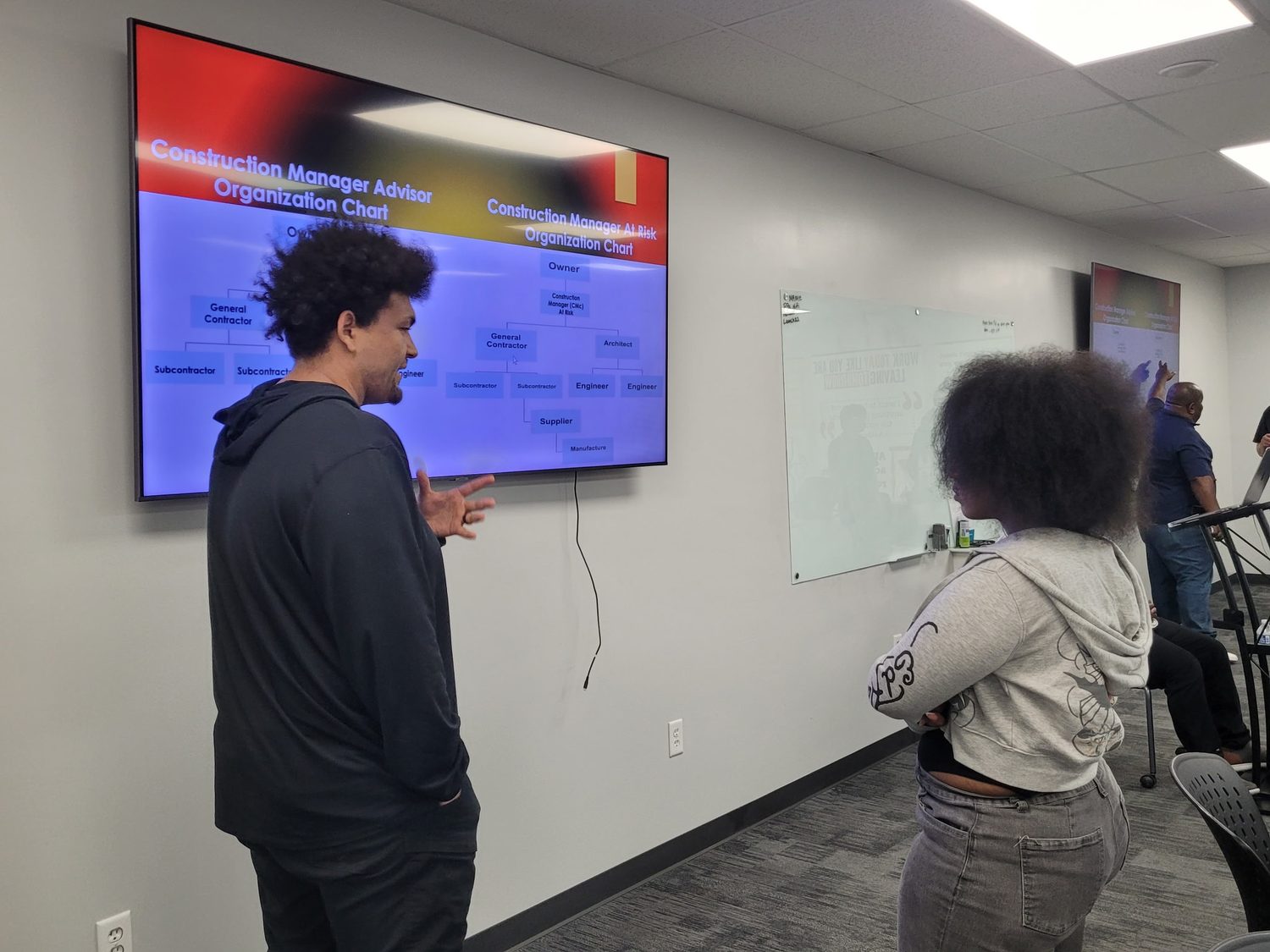 A BTY student and instructor discussing a construction management organization chart shown on screen.