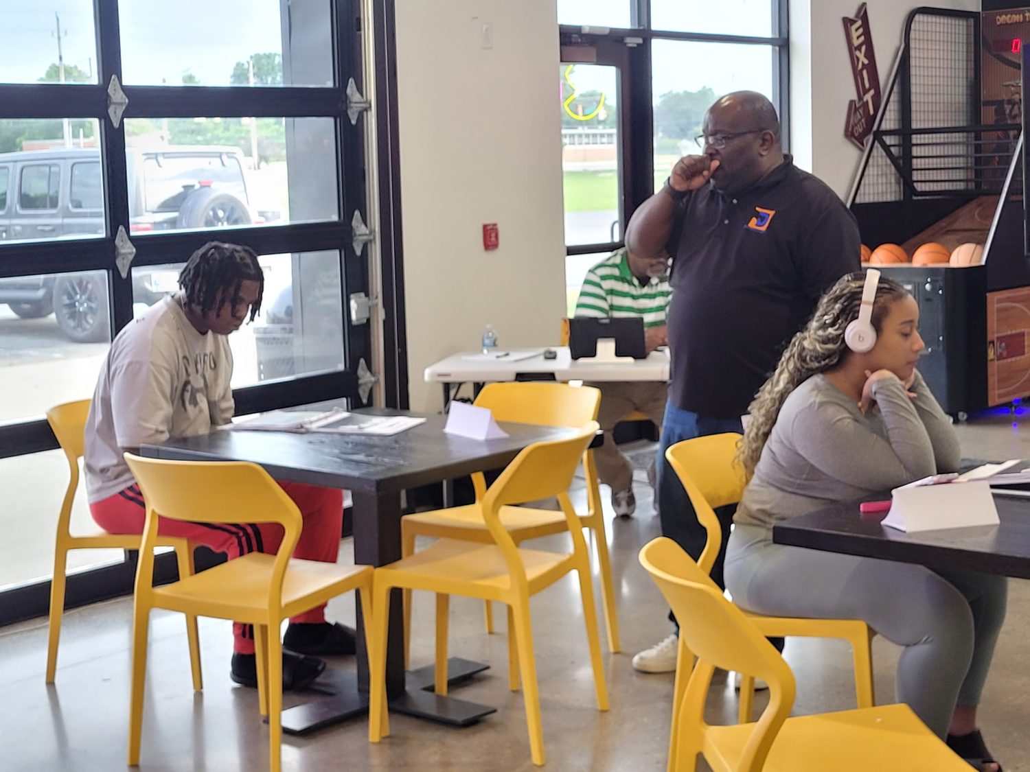 Two BTY students working through printed coursework at tables while an instructor moves through the room.